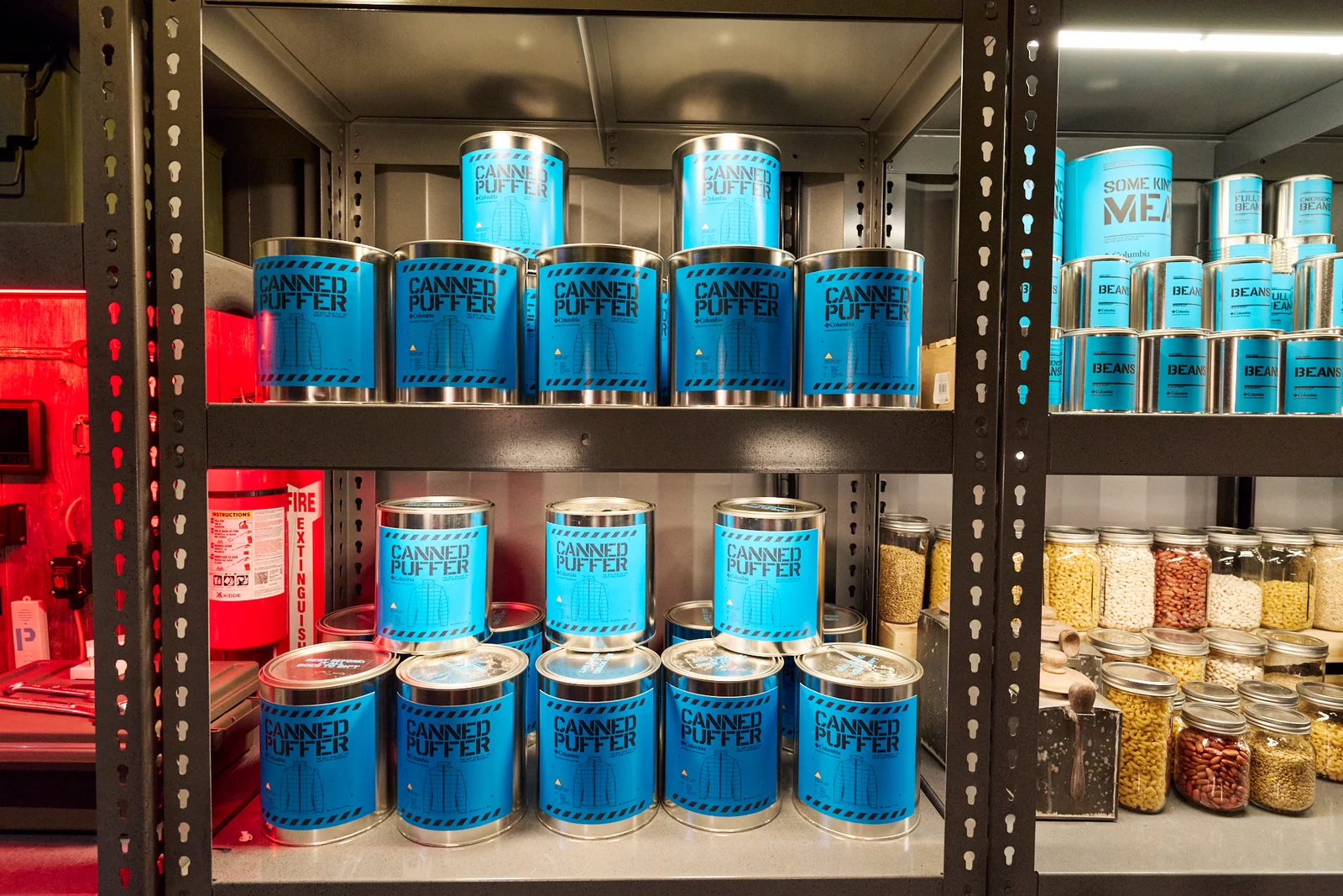 Don’t Panic Room raflarında Columbia montlarının yerleştirildiği mavi Canned Puffer konserve kutuları.